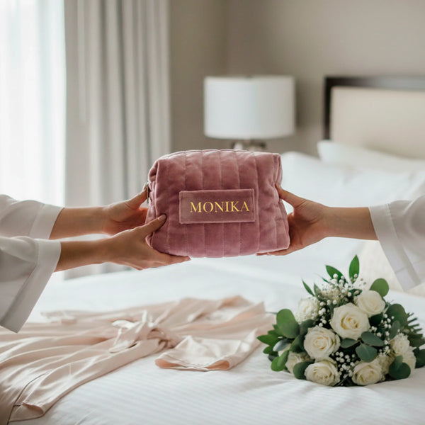 Personalized pink quilted velvet pouch with name, held by two hands over a bed with flowers